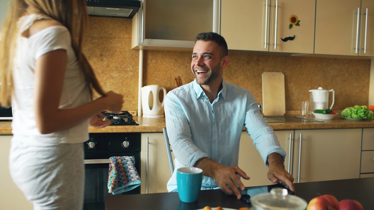 Attractive couple meet in the kitchen early morning kisssing and ebracing then using digital tablet computer for social media surfing at home